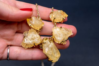 El ele tutuşmuş altın bir kolye ve arka planda bir mücevher..