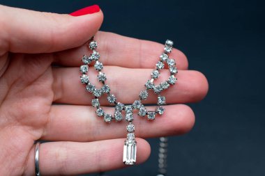 Kırmızı manikürlü bir kadın, sahte elmaslı bir kolye tutuyor.