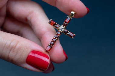 Kırmızı manikürlü bir kadın, arka planda haç tutuyor.