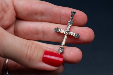 Karanlık bir arka planda haç tutan bir kadının yakın çekimi.