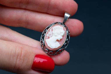 Siyah arka planda gümüş bir kolye tutan bir kadının eli.