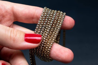 Altın bilezik tutan kırmızı manikürlü bir kadın eli..