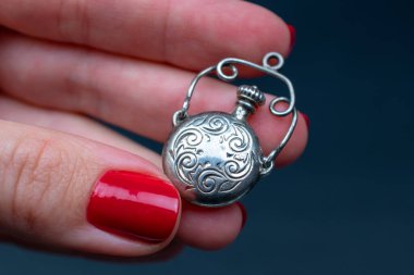 Kırmızı manikürlü kadın elleri gümüş bir noel süsü tutuyor..