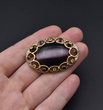 Siyah arka planda değerli bir taşın olduğu bir broşu tutan el..