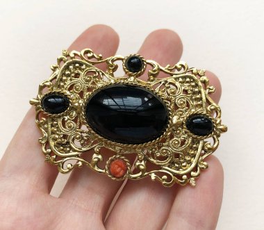 Elinde altın bir broş, beyaz arka planda mücevherler var..