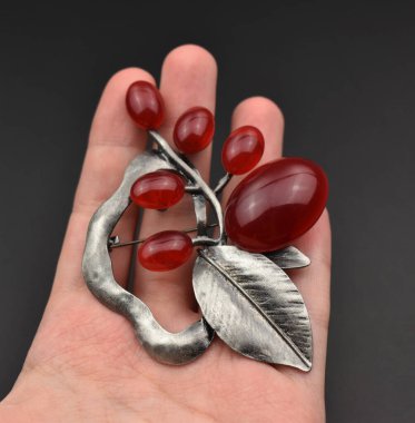 Kırmızı yakutlu ve siyah arka planda gümüş yapraklı bir kolye.