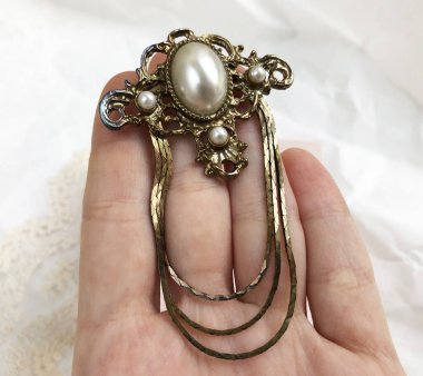 Beyaz arka planda elinde inciler olan altın broş