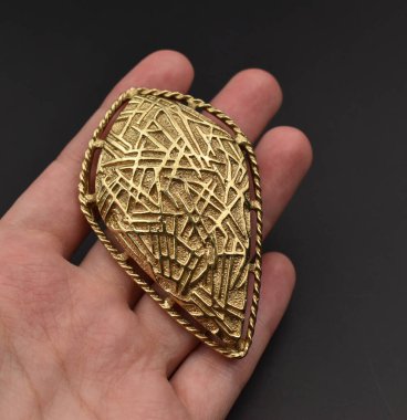 Siyah bir arkaplanda altın bir kolye tutuyor.