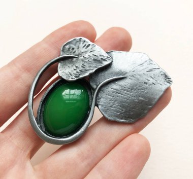 Beyaz arka planda yeşil değerli bir kolye tutuyor..