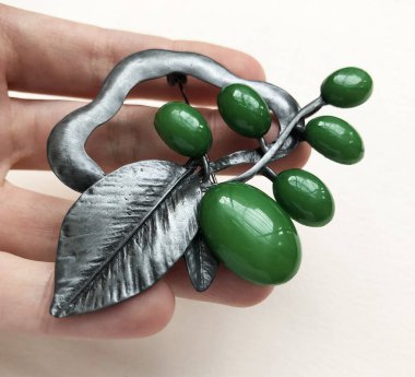 Beyaz arka planda yeşil bir kolye tutuyor.