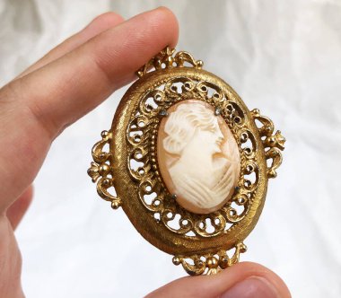 Beyaz arka planda altın bir kolye tutuyor.