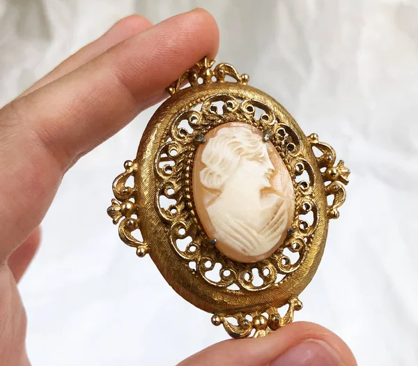 Beyaz arka planda altın bir kolye tutuyor.