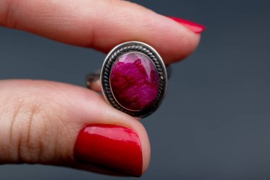 Kırmızı manikürlü, ametist yüzüklü bir kadın eli.