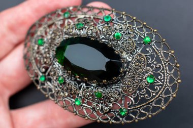 Siyah arka planda yeşil safir bir broş tutuyor.