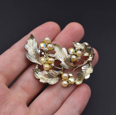 Elinde siyah arka planda incileri olan altın bir broş var.