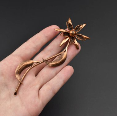 Siyah arka planda çiçek şeklinde çiçek broşu tutan bir el.