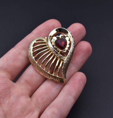 Altın kalp şekilli kolye elinde koyu arkaplanda, yakın plan