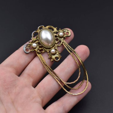 Siyah arka planda incileri olan altın bir kolye tutuyor.