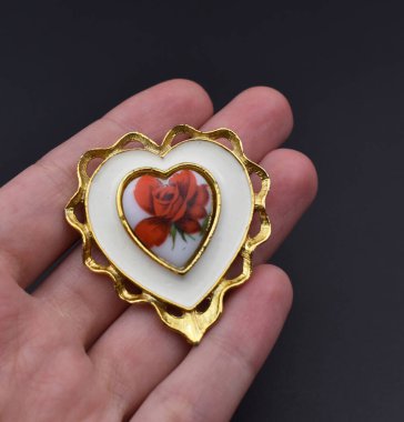 Karanlık bir arka planda, kalp şeklinde bir broşu tutan el..