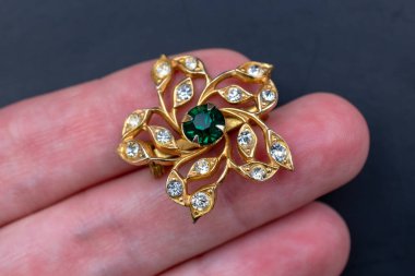 Elinde yeşil zümrüt olan altın bir broş..