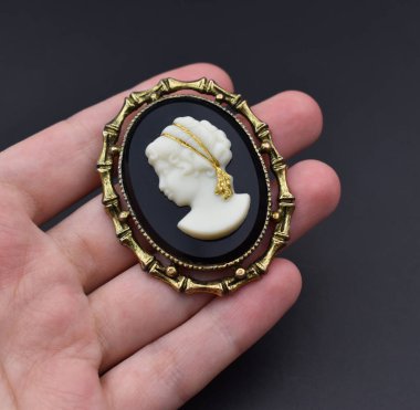 Siyah bir arkaplanda altın bir broş tutan bir kadın.