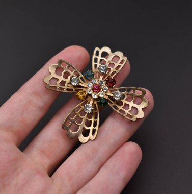 Siyah arka planda güzel bir çiçeğin olduğu bir broşu tutan el.