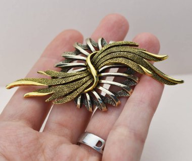 Beyaz arka planda altın bir broş tutuyor, yakın plan.