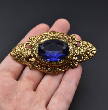 Elinde siyah arka planda mavi safir olan bir broş var.