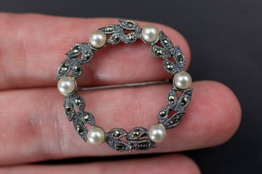 Siyah arka planda elinde inci olan gümüş bir broş..