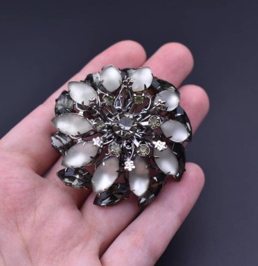 Karanlık bir arka planda değerli taşları olan bir broşu tutan el..