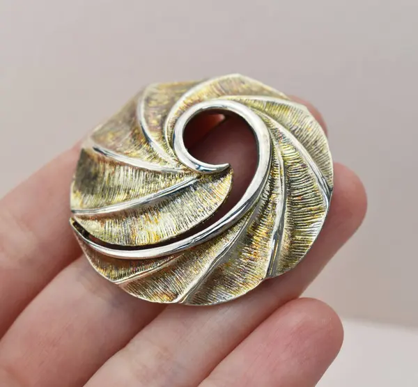 Gri arka planda bir spiral şeklinde bir broş tutuyor.