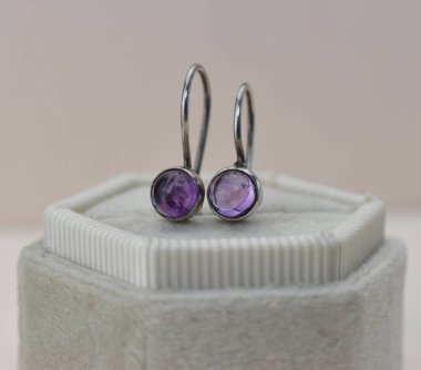 Beyaz arka planda mor ametistli gümüş küpeler.