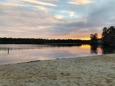 Günbatımı gökyüzü göle, ormana ve nehir manzarasına yansıyor.