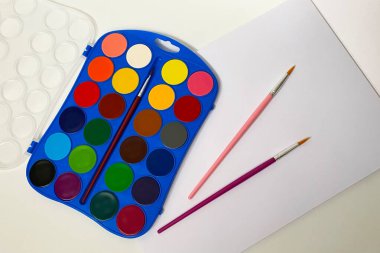 Beyaz arkaplanda suluboya boya ve fırçalar, üst görünüm