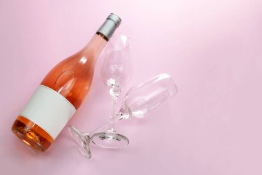 Bir şişe gül şarabı ve pembe arka planda iki boş şarap kadehi.