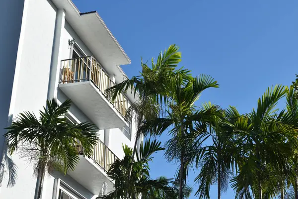 Modern apartment building with palm trees and blue sky in the background.