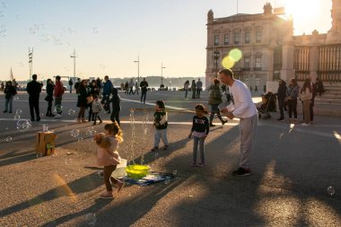 Çocuklar sabun köpüğüyle oynar, mutlu insanlar güneşli bir akşamın keyfini çıkarırlar parkta, Lizbon, Portekiz