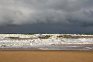 Fırtınalı bulutları, kumlu kumsalı ve dalgaları olan fırtınalı bir deniz.