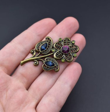 Koyu arkaplanda değerli taşlar olan el ele tutuşan bir broş. Üst görünüm.