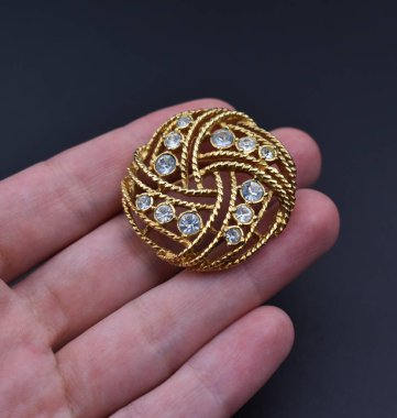 Elinde elmaslarla koyu bir arka planda mücevher broşu..