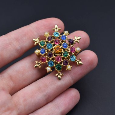 Siyah arka planda değerli taşları olan güzel bir broşu tutan el.