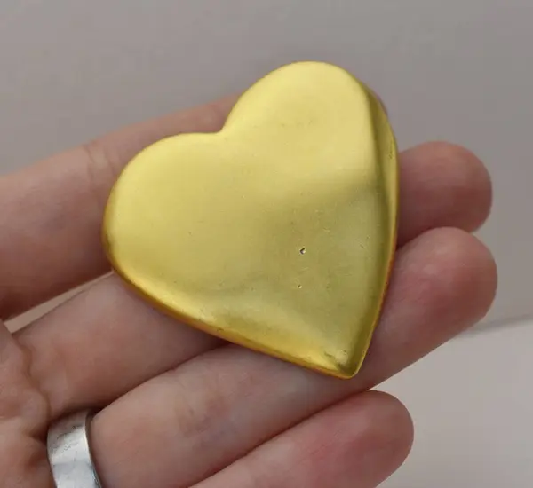 Gold heart in the hand of a girl on a gray background.