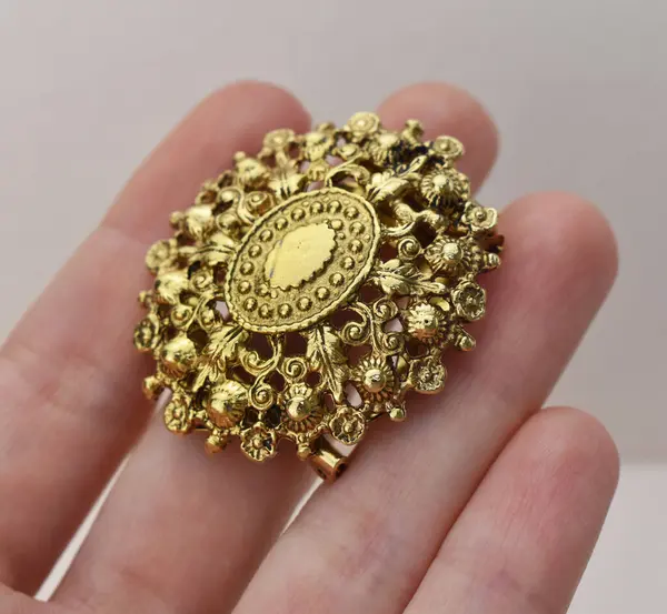 Elinde çiçek şeklinde altın bir broş vardı..