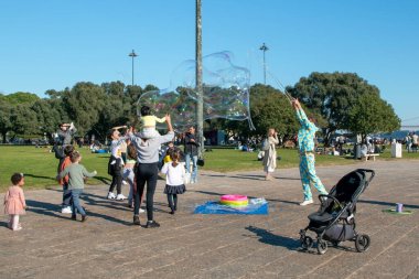 Çocuklar sabun köpüğüyle oynar, mutlu insanlar güneşli bir akşamın keyfini çıkarırlar parkta, Lizbon, Portekiz 