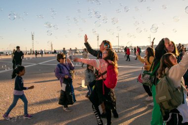 Çocuklar şehrin ana meydanında sabun köpüğüyle oynarlar, mutlu insanlar sıcak güneşli akşamın tadını çıkarırlar, Lizbon, Portekiz