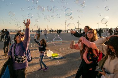 Çocuklar şehrin ana meydanında sabun köpüğüyle oynarlar, mutlu insanlar sıcak güneşli akşamın tadını çıkarırlar, Lizbon, Portekiz
