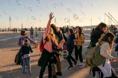 Çocuklar şehrin ana meydanında sabun köpüğüyle oynarlar, mutlu insanlar sıcak güneşli akşamın tadını çıkarırlar, Lizbon, Portekiz