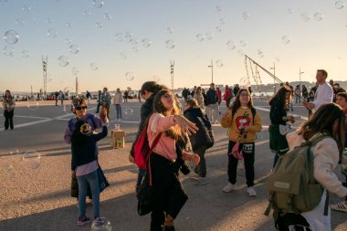 Çocuklar şehrin ana meydanında sabun köpüğüyle oynarlar, mutlu insanlar sıcak güneşli akşamın tadını çıkarırlar, Lizbon, Portekiz