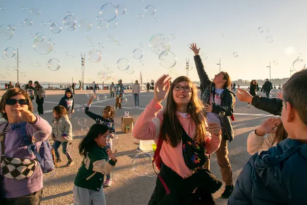 Çocuklar şehrin ana meydanında sabun köpüğüyle oynarlar, mutlu insanlar sıcak güneşli akşamın tadını çıkarırlar, Lizbon, Portekiz