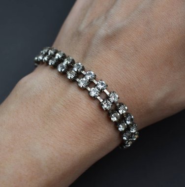 Koyu arkaplanda bir kadının elinde elmas bilezik.